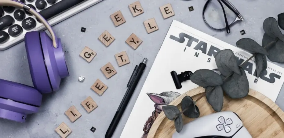 This image has a white keyboard, purple headphones, scrabble letters that spell out geeky lifestyle, a star wars magazine, glasses, and a controller.
